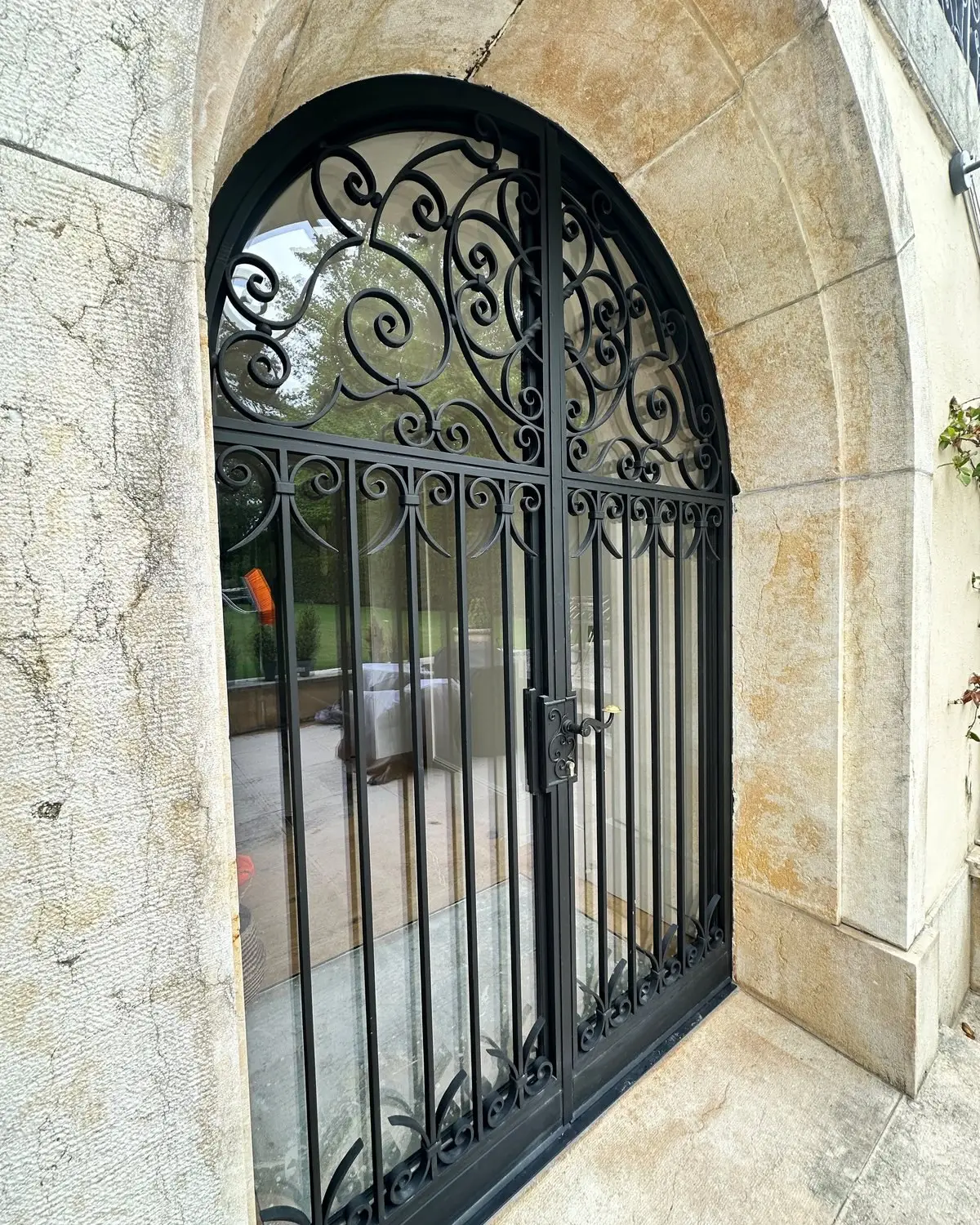 Porte vitrée cintrée derrière une grille en fer forgé, dans un encadrement en pierre